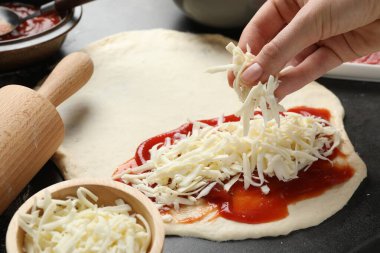 Calzone pizzası yapıyorum. Gri masada hamura peynir ekleyen kadın, yakın plan.