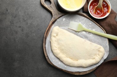 Pişmemiş calzone pizza, sos ve yumurta sarısı gri masada. Metin için boşluk