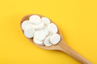 Sarı arka planda kaşıkta antibiyotik haplar, üst manzara.