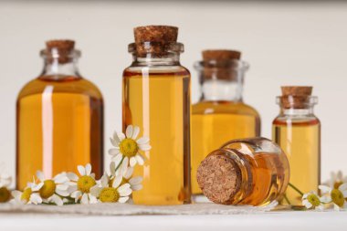 Beyaz ahşap masa üzerinde gerekli yağ ve papatya çiçekleri, yakın plan.