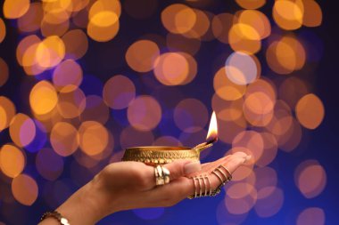 Diwali kutlaması. Renkli arka planda yanan diya lambasını tutan bulanık ışıklı kadın, yakın plan