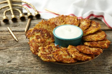 Lezzetli patates krepleri, ekşi krema, menorah ve ahşap masa üzerindeki mumlar, yakın plan. Hanuka bayramı yemekleri.