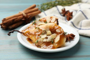 Karamel soslu lezzetli armutlar, mavi ahşap masada badem gevreği ve baharatlar, yakın plan.