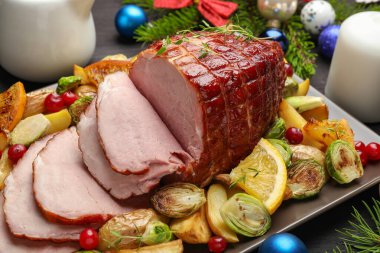 Lezzetli pişmiş jambon, sebze ve portakalla servis edilir. Siyah ahşap masa, yakın plan.