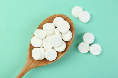 Turkuaz arka planda kaşıkta antibiyotik haplar.