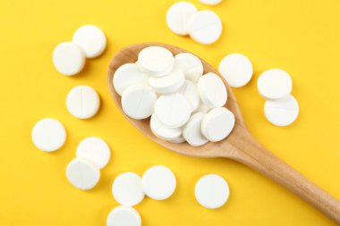 Sarı arka planda kaşıkta antibiyotik haplar, üst manzara.