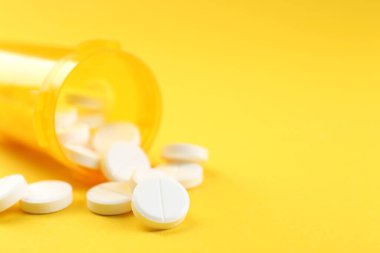 Sarı arka planda antibiyotik hapları olan bir ilaç şişesi, seçici odaklanma. Metin için boşluk