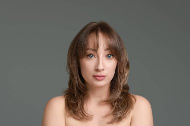 Gri arka planda şık saç kesimi olan çekici bir kadın.