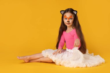 Turuncu arka planda kedi gibi boyalı yüzü ve kulakları olan tatlı bir kız.