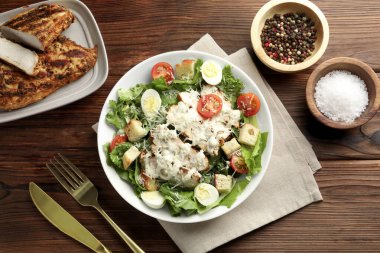 Lezzetli Sezar salatası, tavuklu ve domatesli ahşap masada servis ediliyor.