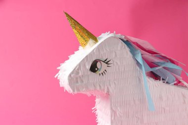 Pembe arka planda tek boynuzlu at şeklinde parlak bir pinata.