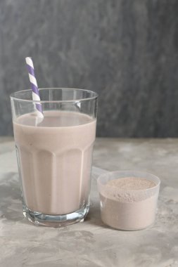 Bardakta leziz protein karışımı ve gri masada toz.