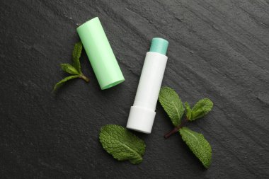 Naneli dudak kremi ve yeşil yapraklar siyah masada, düz yerde. Kozmetik ürünü