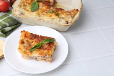 Lezzetli pişmiş lazanya, fesleğenli, beyaz fayanslı masa, yakın plan. Metin için boşluk