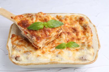 Lezzetli pişmiş lazanya, fesleğenle birlikte beyaz desenli masada, yakın plan.