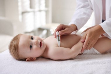 Çocuk doktoru, klinikte termometresi olan küçük çocuğu muayene ediyor. Bebeğin sağlığını kontrol ediyorum.