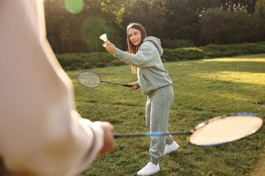 Güneşli bir günde parkta badminton oynayan genç bir kadın ve erkek.