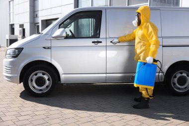 Gri minibüsün yanında sprey tüplü haşere kontrol görevlisi.