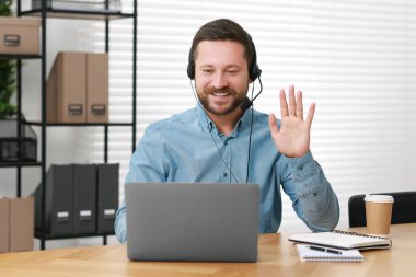 İçerideki ahşap masada bilgisayarla görüntülü konuşma yapan kulaklık yorumcusu.