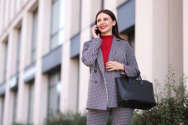 Şık takım elbiseli gülümseyen iş kadını açık havada akıllı telefondan konuşuyor, düşük açılı görüş. Metin için boşluk