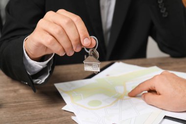 Ahşap masada anahtarı olan bir emlakçı, yakın plan.