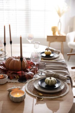 Yemek odasında güzel bulaşık takımları ve sonbahar dekoru olan şık bir masa.