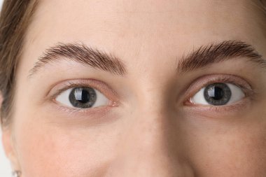 Işıklı arka planda güzel gözleri olan genç bir kadın, yakın plan.