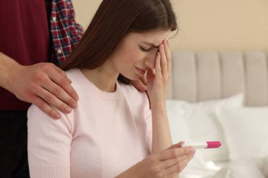 Upset woman with negative pregnancy test indoors. Man supporting his wife at home clipart