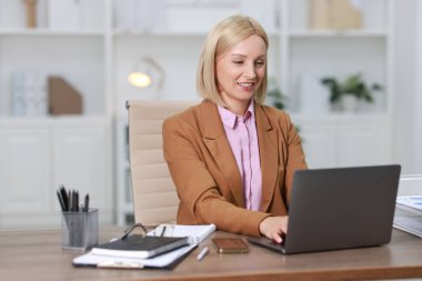 Ofiste dizüstü bilgisayarla çalışan gülümseyen orta yaşlı kadın.