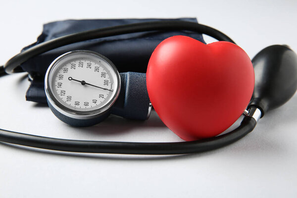 Blood pressure measuring device and squeeze heart on light grey background, closeup