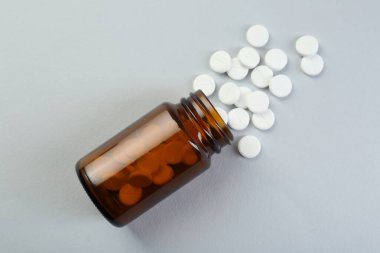 Gri arka planda antibiyotik hapları olan bir ilaç şişesi.