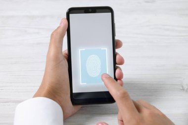 Beyaz ahşap masada akıllı telefonu parmak izi tarayıcısıyla açan adam, yakın plan.