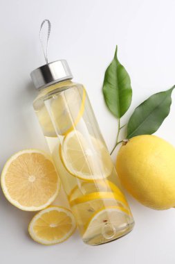 Şişe içinde limon suyu, beyaz arka planda taze meyve ve yapraklar, üst manzara