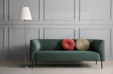 Gri duvarın yanında rahat bir kanepe ve lamba.