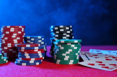Poker fişleri ve iskambil kağıtları pembe masada neon ışıklarda, yakın plan.