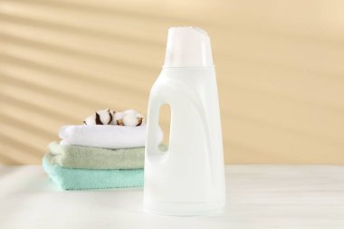 Çamaşır deterjanı şişesi, temiz havlular ve bej arka planda beyaz ahşap masa üzerinde pamuk çiçekler.