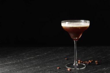 Bir bardak nefis espresso martini ve koyu dokulu masada kahve çekirdekleri. Metin için boşluk