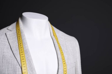 Gri ceketli erkek manken ve siyah arka planda mezura, yakın plan.