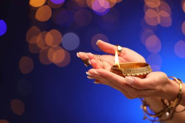 Diwali kutlaması. Mavili arka planda yanan diya lambası tutan kadın, yakın plan.