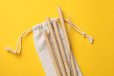 Bambu pipetleri, temizlik fırçası ve sarı arka planda torba, üst görünüm