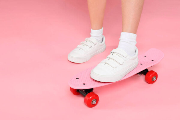 Little girl with penny board on pink background, closeup. Space for text