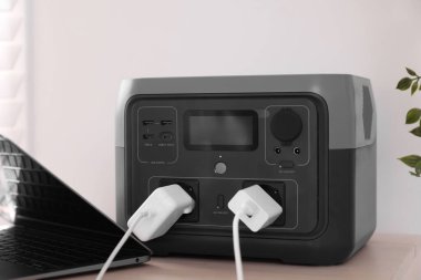 İçerideki ahşap masada taşınabilir elektrik santralinden dizüstü bilgisayar şarj ediliyor.