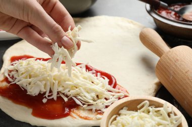 Calzone pizzası yapıyorum. Gri masada hamura peynir ekleyen kadın, yakın plan.