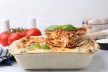 Lezzetli pişmiş lazanya, fesleğenle birlikte beyaz desenli masada, yakın plan.