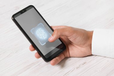 Beyaz ahşap masada akıllı telefonu parmak izi tarayıcısıyla açan adam, yakın plan.