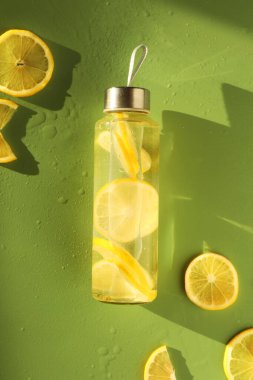Limonlu su şişede ve dilimler ıslak yeşil arka planda, düz yerde