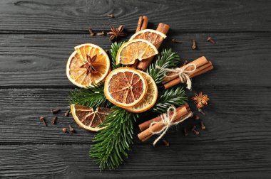 Farklı baharatlar, kurutulmuş portakal dilimleri ve siyah ahşap masa üzerinde köknar ağacı dalları, düz bir yer. Noel sezonu