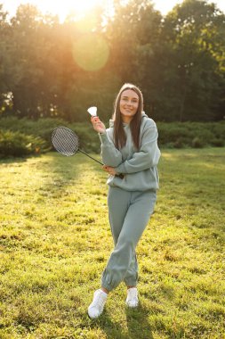 Güneşli bir günde parkta badminton raketi ve pipisi olan mutlu genç bir kadın.