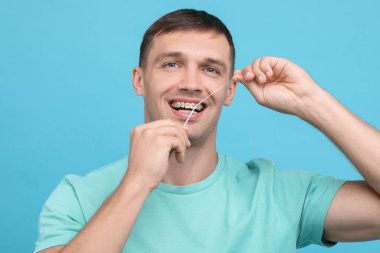 Diş teli temizleyen bir adam açık mavi arka planda diş ipi kullanıyor.