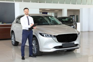 Salondaki yeni gümüş arabanın yanındaki mutlu satıcı.